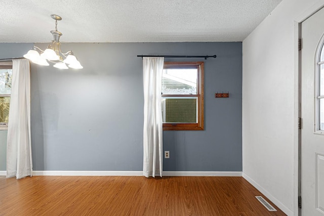 unfurnished room featuring wood-type flooring, an inviting chandelier, and a textured ceiling