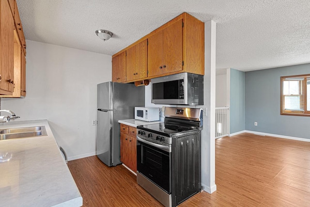 kitchen featuring light wood-type flooring, stainless steel appliances, a textured ceiling, and sink