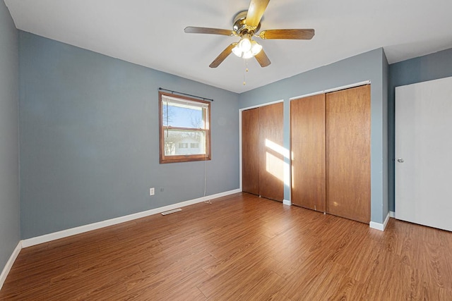 unfurnished bedroom featuring ceiling fan, multiple closets, and light wood-type flooring