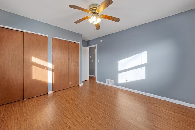 unfurnished bedroom featuring ceiling fan, two closets, and light hardwood / wood-style floors