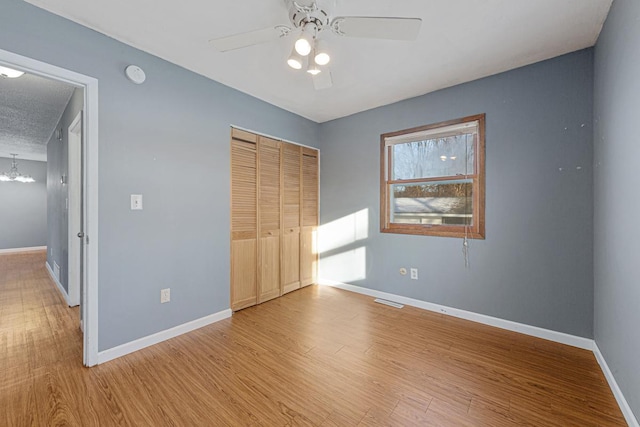 unfurnished bedroom featuring ceiling fan with notable chandelier, a textured ceiling, a closet, and light wood-type flooring