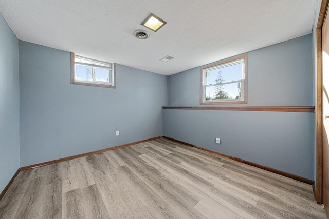 basement with light wood-type flooring, a wealth of natural light, and a textured ceiling