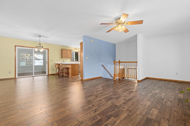 unfurnished living room with a textured ceiling, ceiling fan with notable chandelier, and dark hardwood / wood-style floors