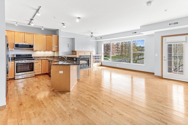 kitchen featuring sink, light hardwood / wood-style flooring, dark stone countertops, appliances with stainless steel finishes, and kitchen peninsula