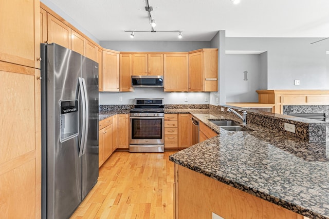 kitchen with sink, light hardwood / wood-style flooring, kitchen peninsula, dark stone countertops, and appliances with stainless steel finishes