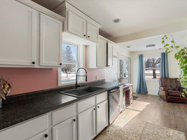 kitchen with white cabinetry, sink, dark stone counters, stainless steel dishwasher, and light wood-type flooring