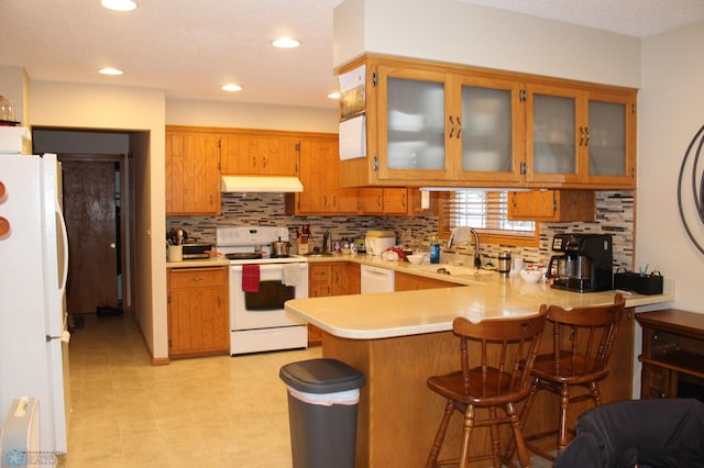 kitchen with sink, white appliances, a kitchen breakfast bar, tasteful backsplash, and kitchen peninsula