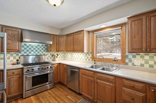 kitchen with appliances with stainless steel finishes, sink, light wood-type flooring, wall chimney range hood, and a textured ceiling