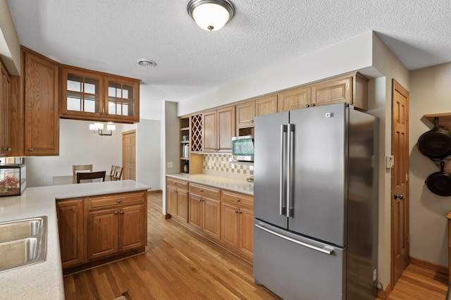 kitchen featuring sink, light wood-type flooring, kitchen peninsula, stainless steel appliances, and decorative backsplash