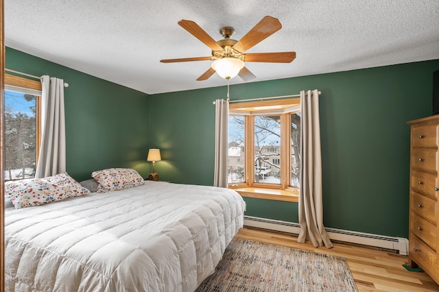 bedroom featuring ceiling fan, a baseboard heating unit, hardwood / wood-style floors, and a textured ceiling