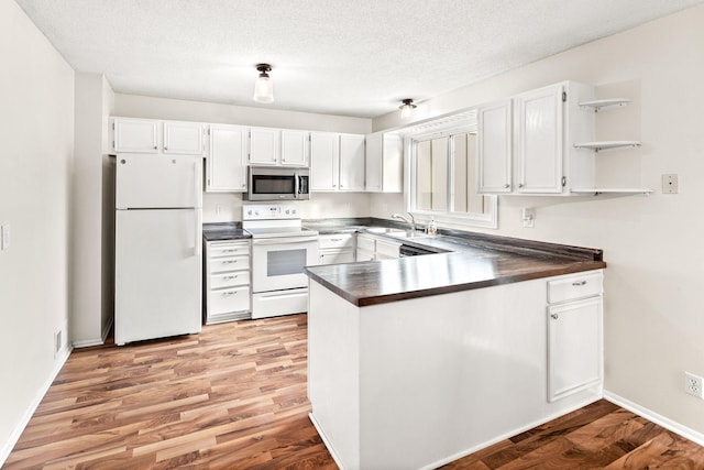 kitchen with a textured ceiling, white cabinets, white appliances, and light hardwood / wood-style floors