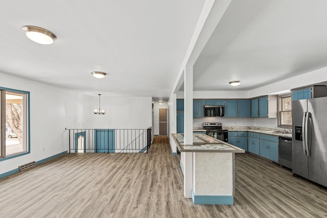 kitchen with appliances with stainless steel finishes, blue cabinets, wood-type flooring, hanging light fixtures, and an inviting chandelier