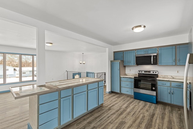 kitchen featuring decorative light fixtures, wood-type flooring, kitchen peninsula, stainless steel appliances, and blue cabinetry