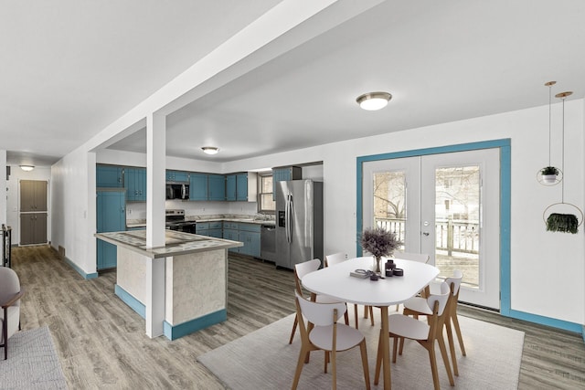 kitchen with hanging light fixtures, light wood-type flooring, blue cabinetry, and appliances with stainless steel finishes