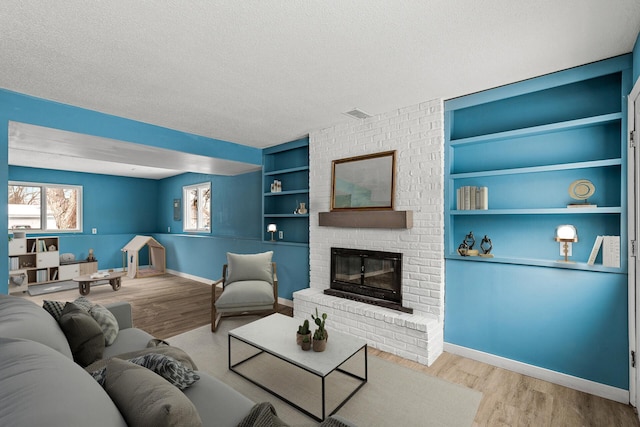 living room with light hardwood / wood-style flooring, a textured ceiling, a fireplace, and built in shelves