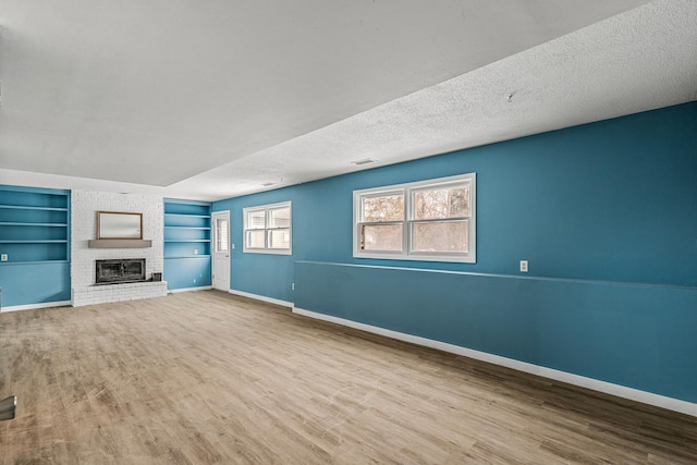 unfurnished living room with built in shelves, a fireplace, light hardwood / wood-style floors, and a textured ceiling