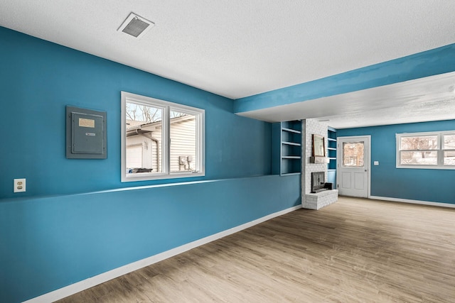 empty room with hardwood / wood-style flooring, a fireplace, built in features, and a textured ceiling