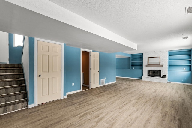 unfurnished living room with hardwood / wood-style flooring, a fireplace, built in features, and a textured ceiling