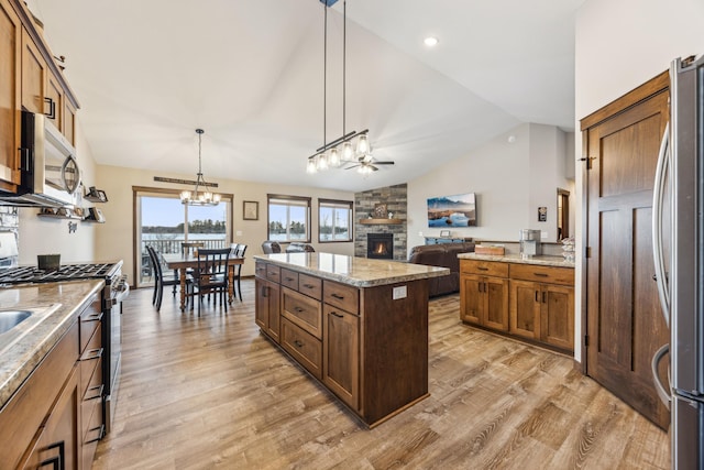 kitchen featuring a stone fireplace, appliances with stainless steel finishes, hanging light fixtures, vaulted ceiling, and a center island