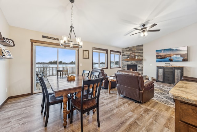 dining room with lofted ceiling, ceiling fan with notable chandelier, hardwood / wood-style floors, and a stone fireplace