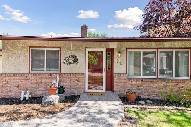 doorway to property featuring brick siding, a chimney, and stucco siding