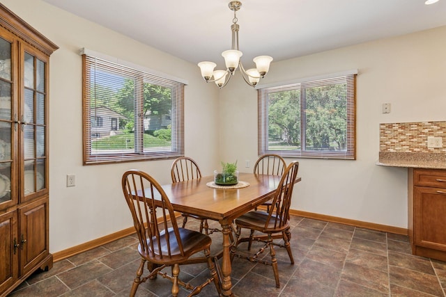 dining room featuring a chandelier, baseboards, and dark stone finish flooring