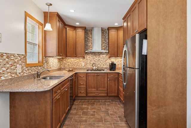 kitchen featuring appliances with stainless steel finishes, wall chimney range hood, brown cabinets, a sink, and light stone counters