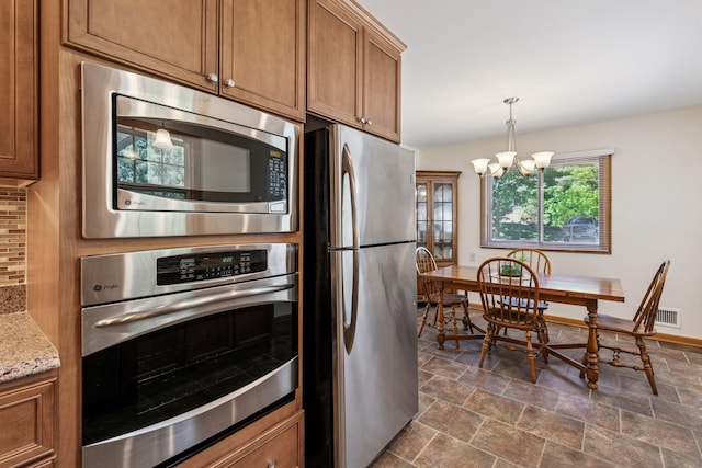 kitchen featuring appliances with stainless steel finishes, brown cabinetry, dark stone finish flooring, and decorative backsplash