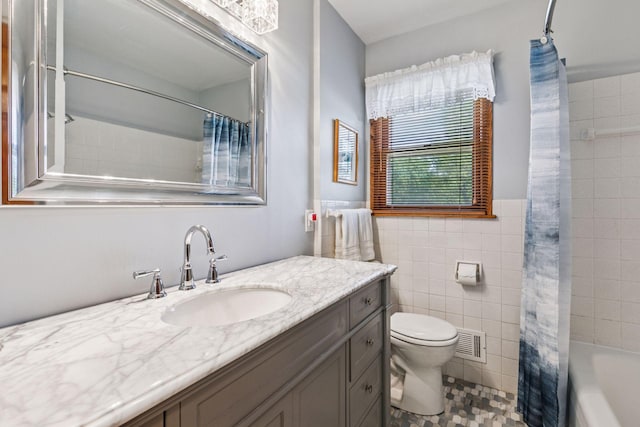 bathroom with toilet, vanity, tile walls, tile patterned flooring, and wainscoting