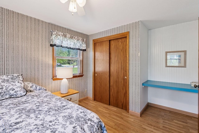 bedroom featuring wood finished floors, wallpapered walls, baseboards, a closet, and a ceiling fan