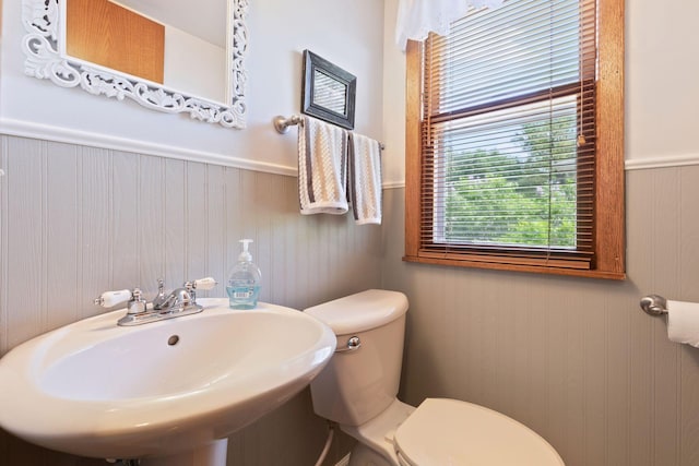 bathroom featuring a sink, a wainscoted wall, toilet, and wood walls