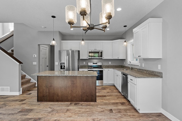 kitchen with stainless steel appliances, a kitchen island, a sink, white cabinets, and hanging light fixtures