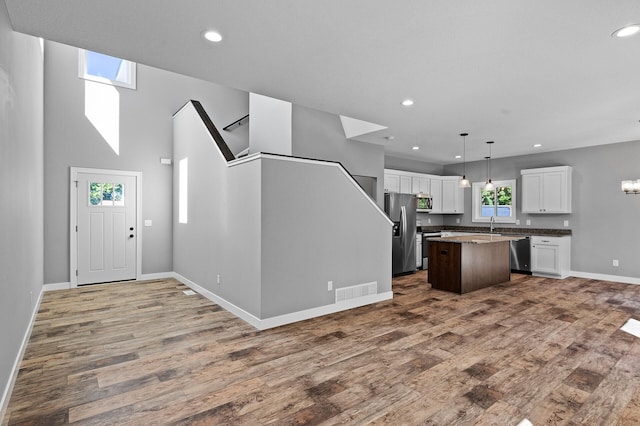 kitchen featuring white cabinets, a kitchen island, appliances with stainless steel finishes, open floor plan, and hanging light fixtures