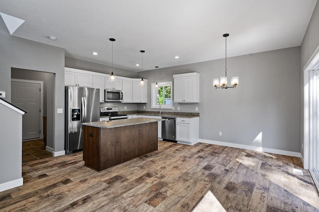 kitchen featuring appliances with stainless steel finishes, white cabinetry, a kitchen island, and hanging light fixtures