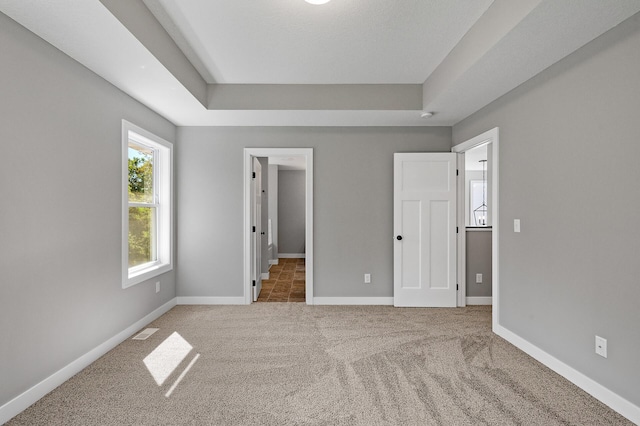 unfurnished bedroom featuring carpet floors, a raised ceiling, visible vents, and baseboards