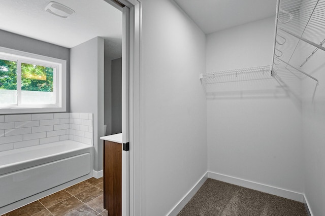 bathroom with a washtub, a walk in closet, vanity, and baseboards