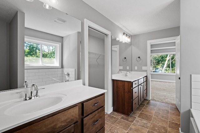 bathroom featuring two vanities, a sink, a walk in closet, and a healthy amount of sunlight