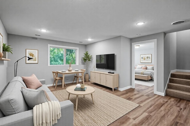 living room featuring stairway, baseboards, visible vents, and wood finished floors