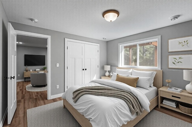 bedroom featuring dark wood-style floors, a textured ceiling, baseboards, and a closet