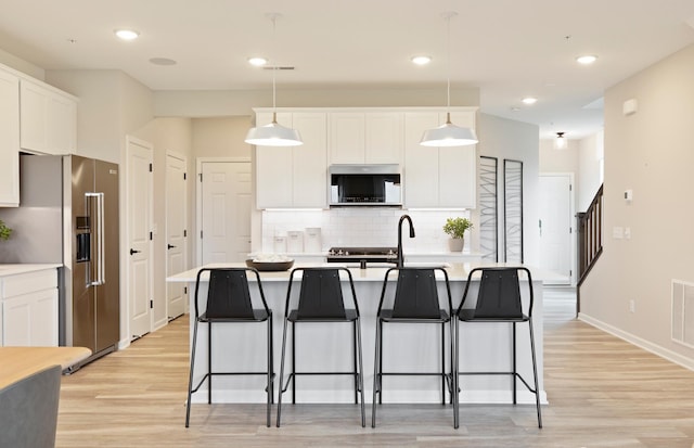 kitchen featuring appliances with stainless steel finishes, white cabinetry, a kitchen island with sink, and pendant lighting