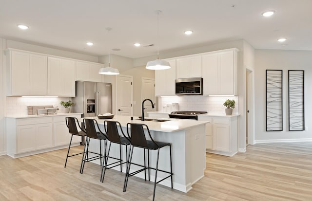 kitchen with white cabinetry, sink, decorative light fixtures, a kitchen island with sink, and appliances with stainless steel finishes