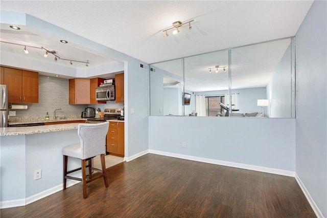 kitchen featuring a kitchen breakfast bar, decorative backsplash, dark hardwood / wood-style flooring, kitchen peninsula, and stainless steel appliances