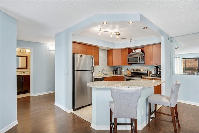 kitchen featuring a kitchen bar, light hardwood / wood-style flooring, a textured ceiling, appliances with stainless steel finishes, and light stone counters