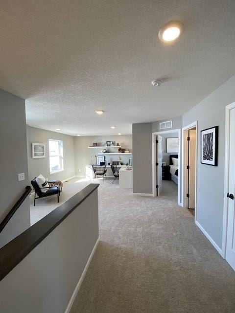 hall with a textured ceiling and light colored carpet