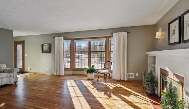 living room featuring wood-type flooring, a brick fireplace, and a textured ceiling