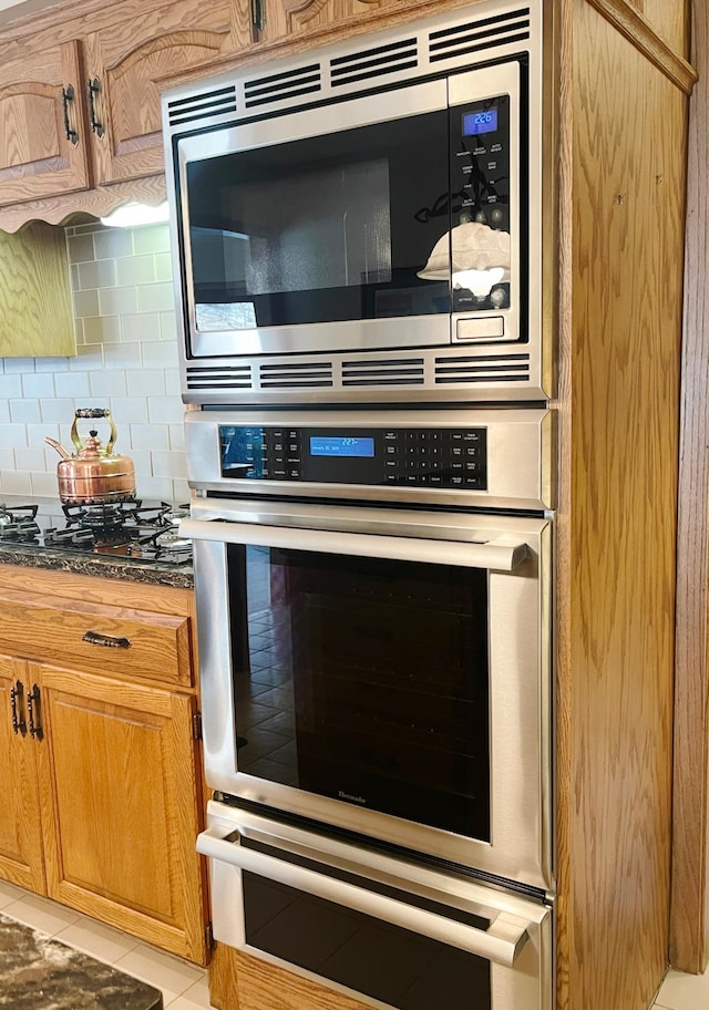 kitchen featuring stainless steel appliances, dark stone countertops, light tile patterned floors, and backsplash