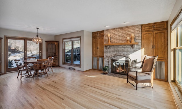 interior space with a brick fireplace, a healthy amount of sunlight, an inviting chandelier, and light wood-type flooring