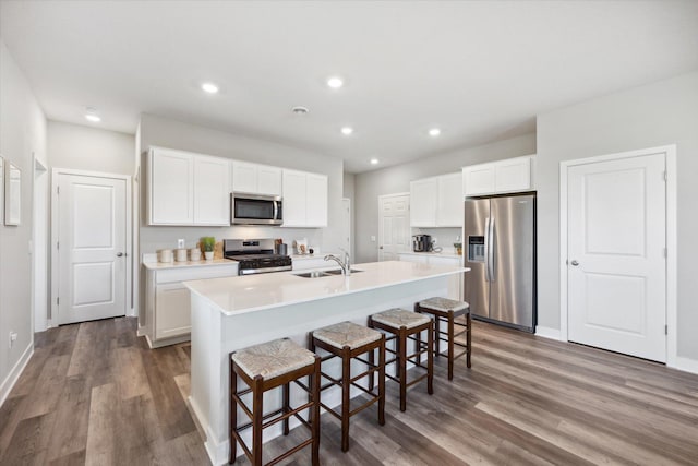 kitchen with appliances with stainless steel finishes, wood finished floors, a center island with sink, and a sink
