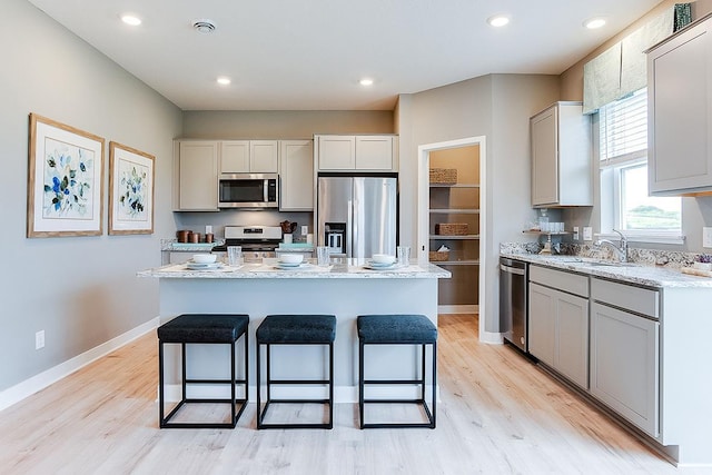 kitchen with light stone counters, a center island, stainless steel appliances, and light wood-type flooring