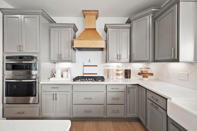 kitchen featuring gray cabinetry, tasteful backsplash, light wood-type flooring, appliances with stainless steel finishes, and custom exhaust hood